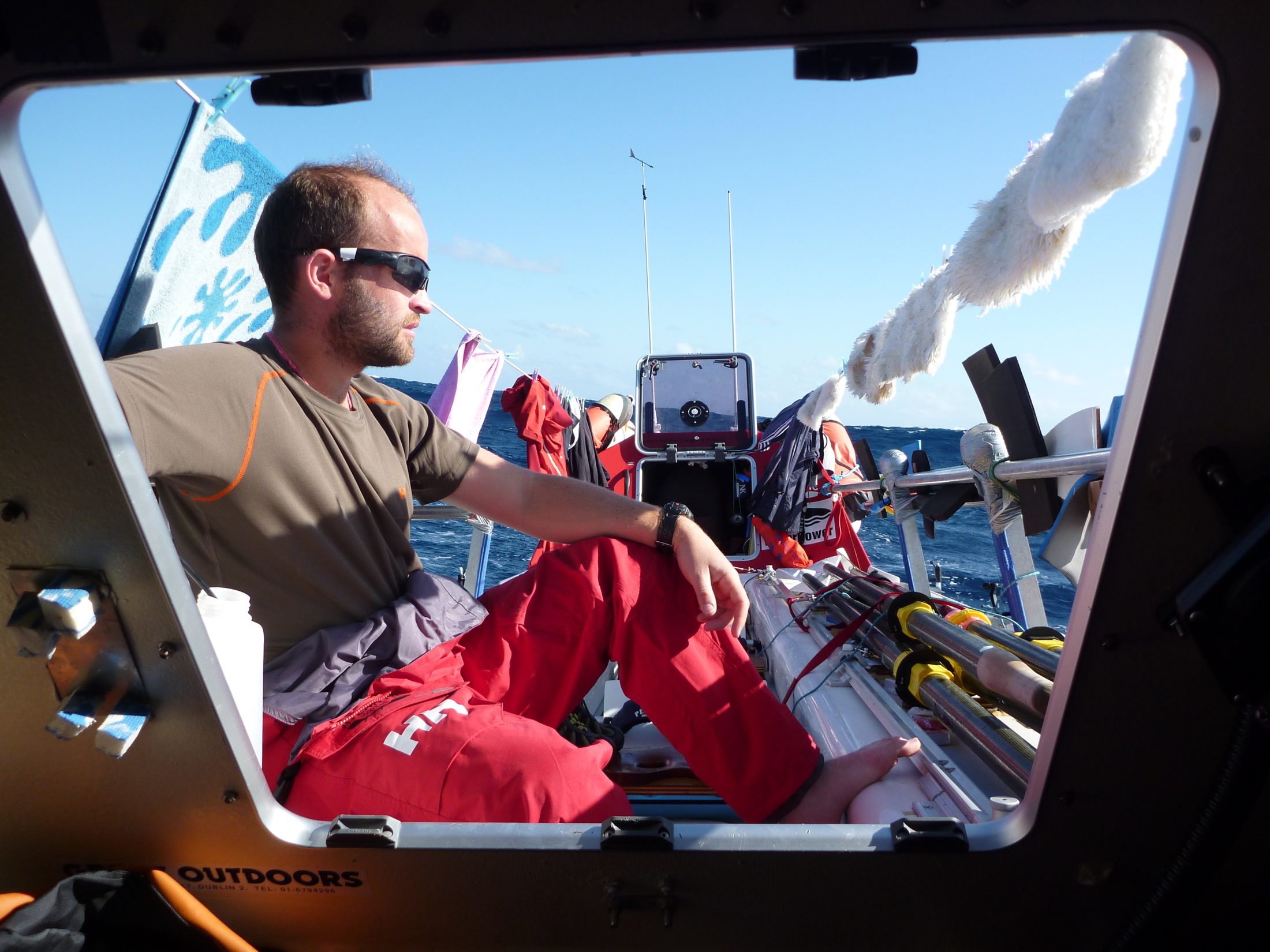 Mike Jones mid-row on the Atlantic crossing, framed through the boat's cabin hatch