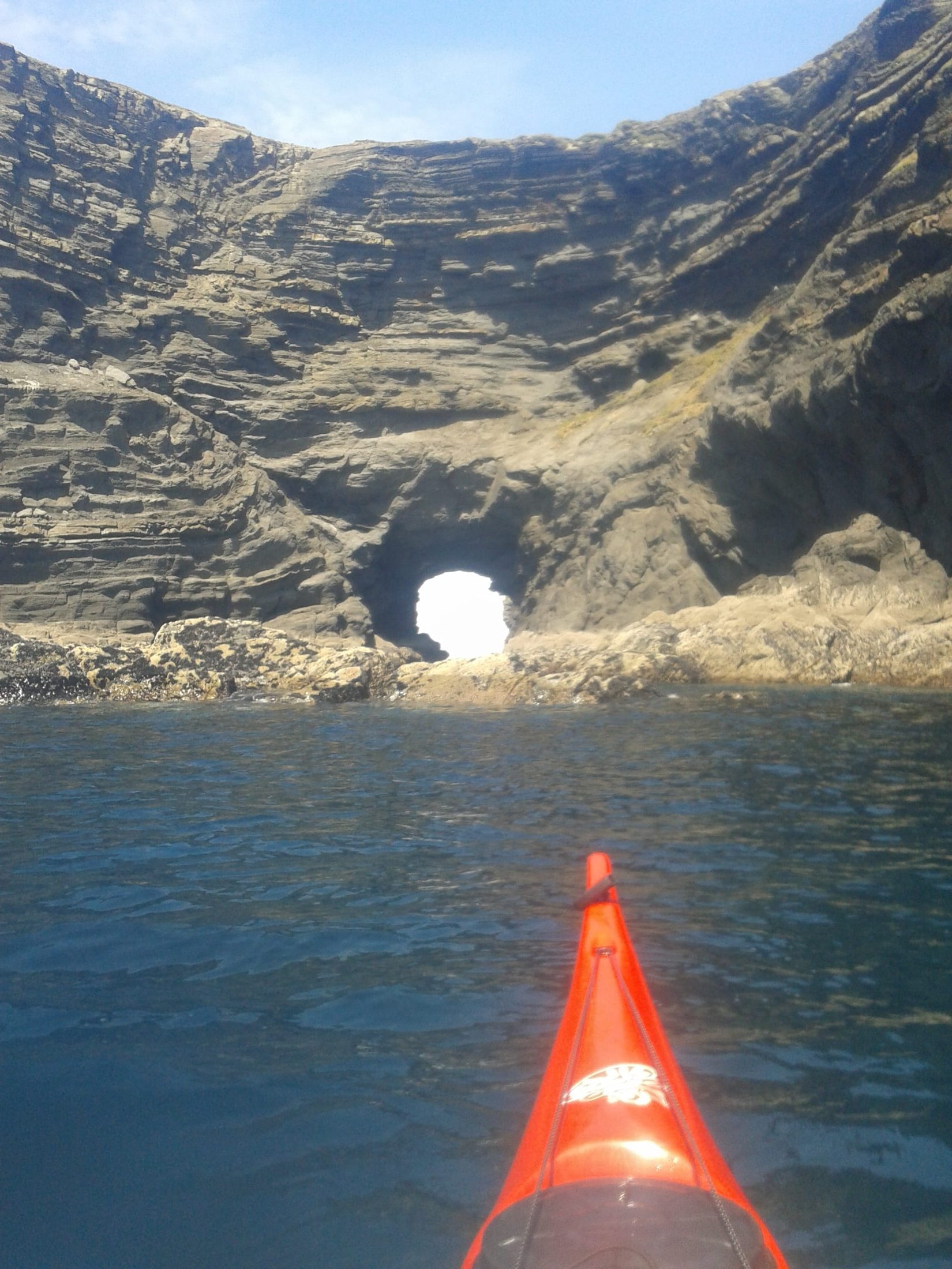 Sea kayak approaching a cave arch in dramatic sea cliffs